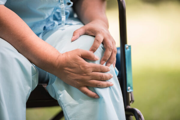 Image of an elderly woman sitting on a wheelchair while clutching her knees due to joint pain