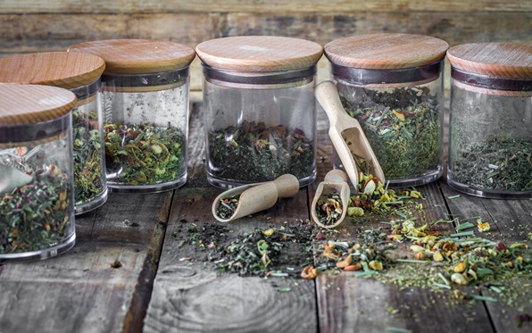 still life of loose tea in glass jar and wooden spoons on wooden background